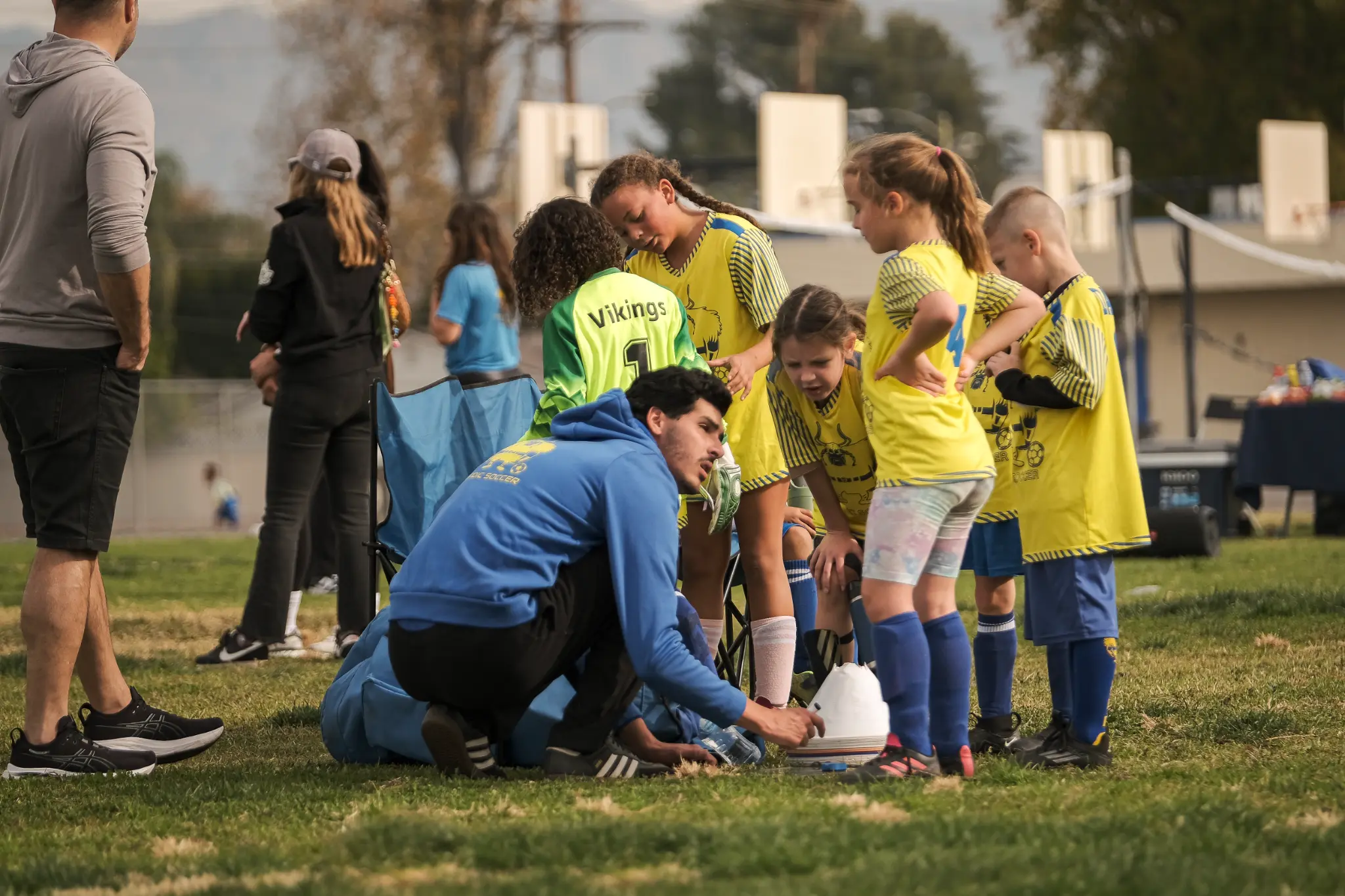 Nordic Soccer youth players in blue and yellow jerseys during team huddle with coach at Carpenter Community Charter field in Studio City
